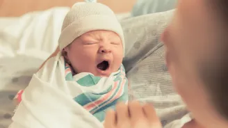 Newborn baby yawning in it's mother's arms