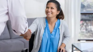 A woman in a wheelchair is shaking hands with a doctor.