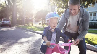 Father teaching his young daughter how to ride a pink bike in the street.
