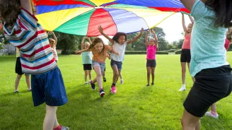 A group of children outside playing with a large multicolored parachute.