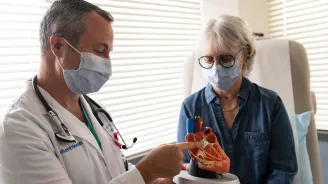 Doctor showing a woman patient a heart model while both wear masks.