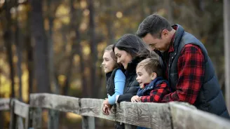 A family of four leaning on a fence while outdoors in the winter.
