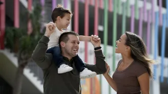 A child riding on his fathers shoulders while his smiling mother walks along side.