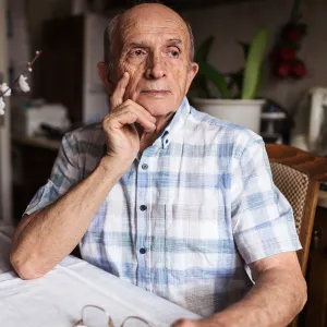 A Man Looks Seriously Out a Window of His Home