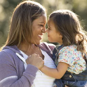 A mother smiles at her young daughter while holding her. 