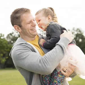 A Caucasian father and his young daughter play in the park together.