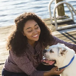 A young African American women plays with her dog on a dock by the lake.