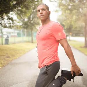 An African American man stretches his legs before running in the park.