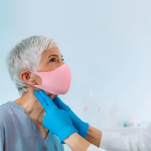A Doctor examines a patient's neck while they both wear face coverings
