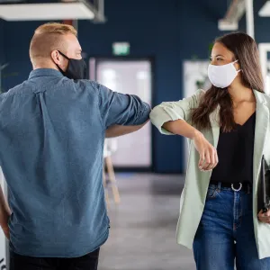 co-workers elbowing hello in the office while wear facemasks