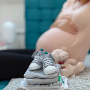 A picture of a set of baby clothes folded next to a pregnant mother