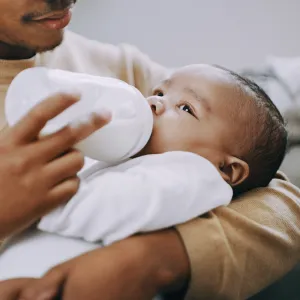 A Father Bottle Feeds His Baby Who is Swaddled in His Arms.