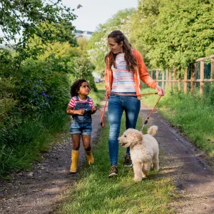 A Mother and Daughter Walk Their Labradoodle on a Country Road.