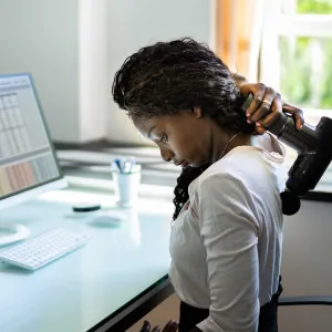 A woman using a massage gun on her back