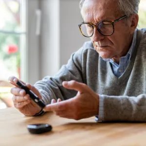 A Senior Checks His Glucose Levels with a Device While Sitting at the Kitchen Table