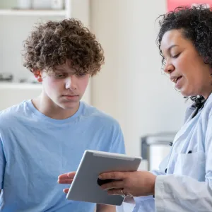 A Physician Goes Over a Teenager's Chart on a Tablet