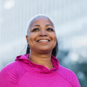 A smiling woman outside wearing a pink shirt for breast cancer awareness.