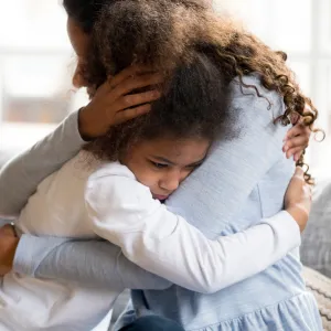 A Mother Hugs Her Sad Daughter on the Couch at Home.