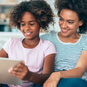 A MOther and Daughter Smile as They Sit Together and Surf the Internet on a Tablet.