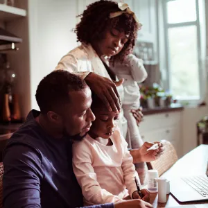 A Family Huddles Around a Laptop to Participate in a Video Visit with a Physician.
