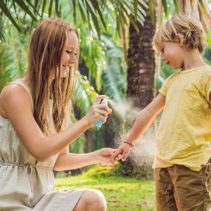 A Mother Sprays Her Young Son with Bug Spray in a Park