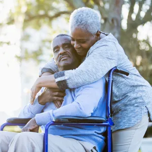 A Woman Embraces Her Husband as He Sits in a Wheelchair Outdoors in a Park