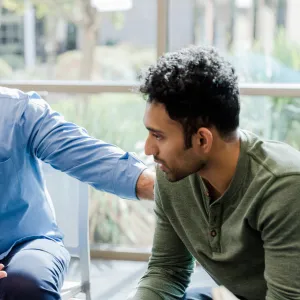 A Therapist Speaks to His Patient and Put's his Hand on His Shoulder