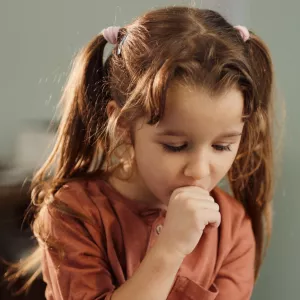 A Little Girl in Pig Tails Covers Her Mouth While Coughing