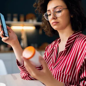 A Woman Looks at a Bottle While Researching it on Her Phone.