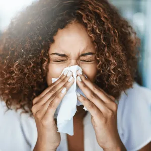 A Woman Sneezes into a Tissue at Home