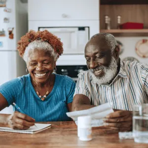 Man and Woman Sitting at Table Tracking Medications in Notebook