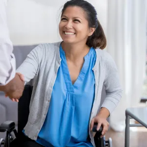 A woman in a wheelchair is shaking hands with a doctor.