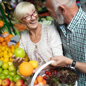 A senior couples shopping for produce with a basket.