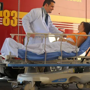 Woman arriving in a stretcher from ambulance with a doctor by her side.