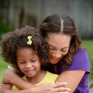 A mother hugs her daughter from behind.