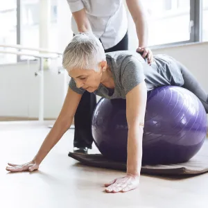 A Caucasian woman balances herself on an exercise ball.