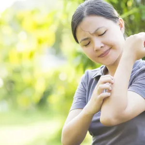 A woman scratches an itchy rash on her arm.