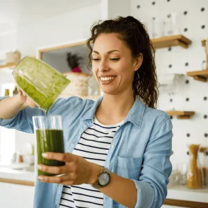 A woman pouring a green smoothie into a cup.