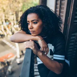A Woman With a Concerned Look on Her Face Stares at Street From Her Balcony.