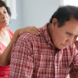 A woman rests her hand on her husband's back.
