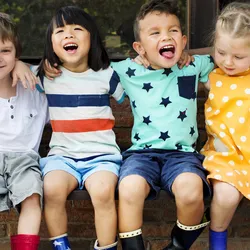 A happy group of children sit on a bench outdoors.