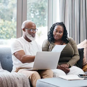 Man and woman reviewing paperwork with computer on lap