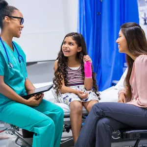Child with a cast on her arm is sitting with a doctor and her mother