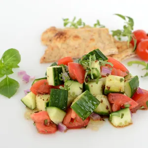 Mound of cucumber salad with pita and tomato garnishes