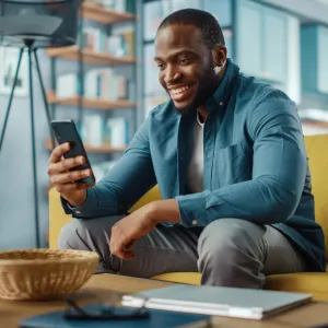 A smiling man looking at his phone while sitting on a couch