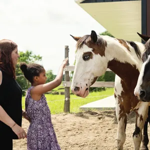 Daughter petting horse with mother behind her