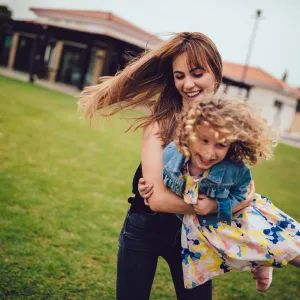 Mom spins her young daughter around in the grass