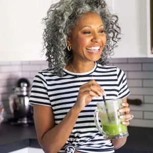 A woman drinking a healthy green smoothie in her kitchen.