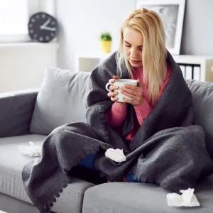 A woman drinking tea under a blanket at home.