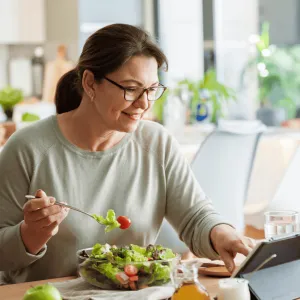 A woman eating a health meal while reading on a tablet.